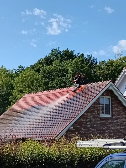 Einsatzfoto von ExpertRinnen: Mitarbeiter auf dem First eines Ziegeldachs, Sprühnebel vor dunklen Bäumen