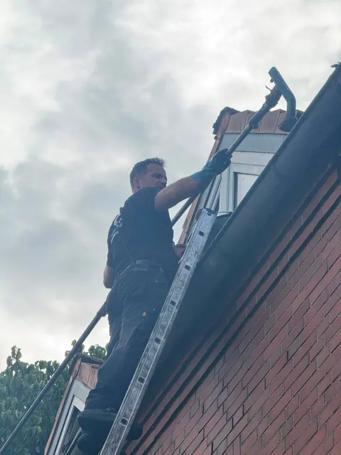 Einsatzfoto von ExpertRinnen: Mitarbeiter auf der Leiter reinigt die Dachrinne an einer Klinkerfassade
