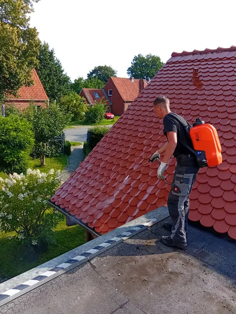 Einsatzfoto von ExpertRinnen: Mitarbeiter mit orangem Rückensprühgerät auf einem Biberschwanzdach