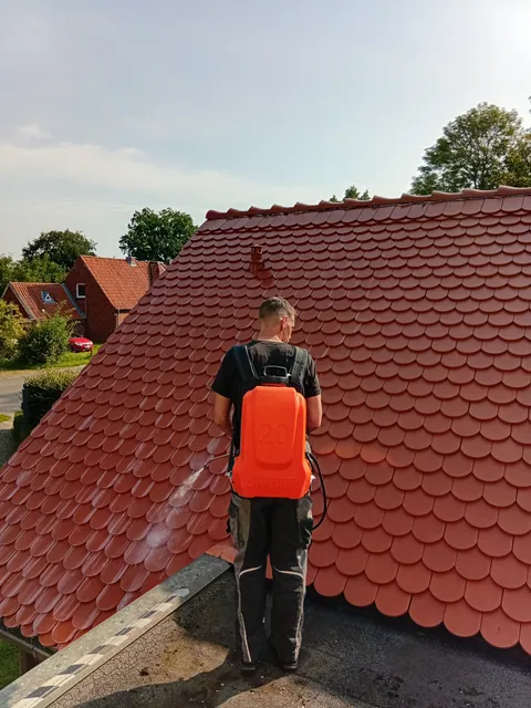 Einsatzfoto von ExpertRinnen: Mitarbeiter von hinten mit orangem Rückensprühgerät vor einem frisch gereinigten Ziegeldach